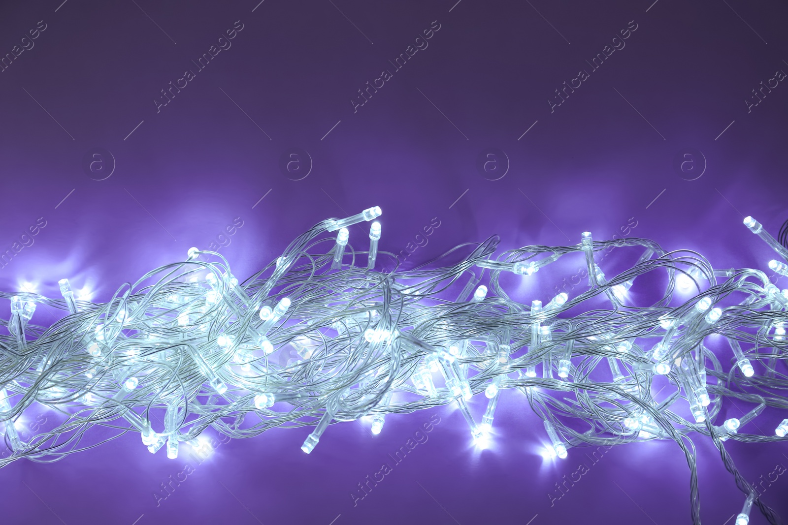 Photo of Glowing Christmas lights on dark violet background, top view. Space for text