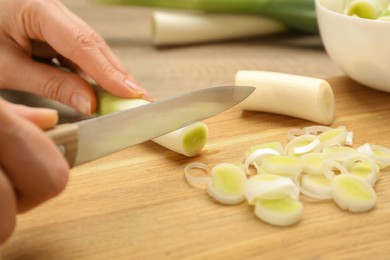 Photo of Woman cutting fresh raw leek on wooden board, closeup