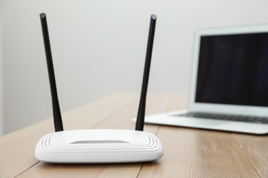 Photo of Modern Wi-Fi router and laptop on wooden table indoors