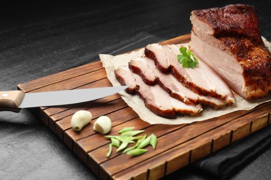 Photo of Pieces of baked pork belly served with parsley and garlic on black textured table