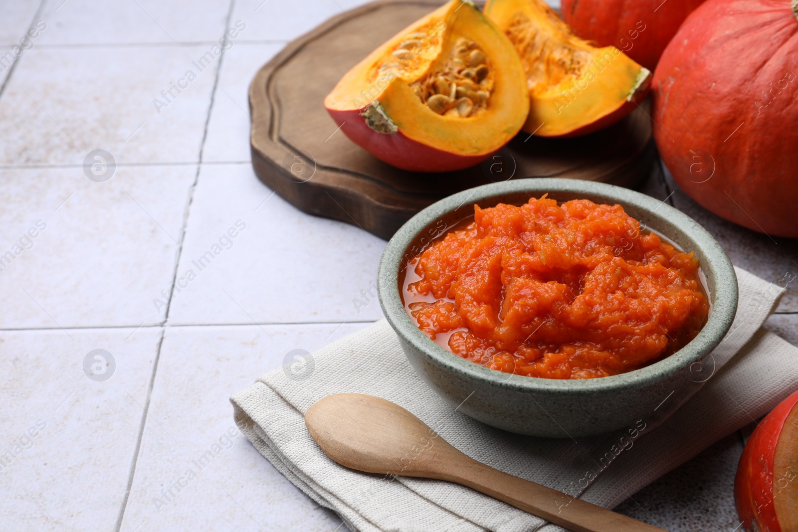 Photo of Bowl of delicious pumpkin jam and fresh pumpkin on tiled surface, space for text