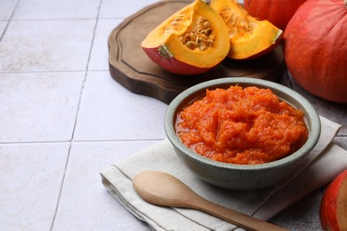 Photo of Bowl of delicious pumpkin jam and fresh pumpkin on tiled surface, space for text