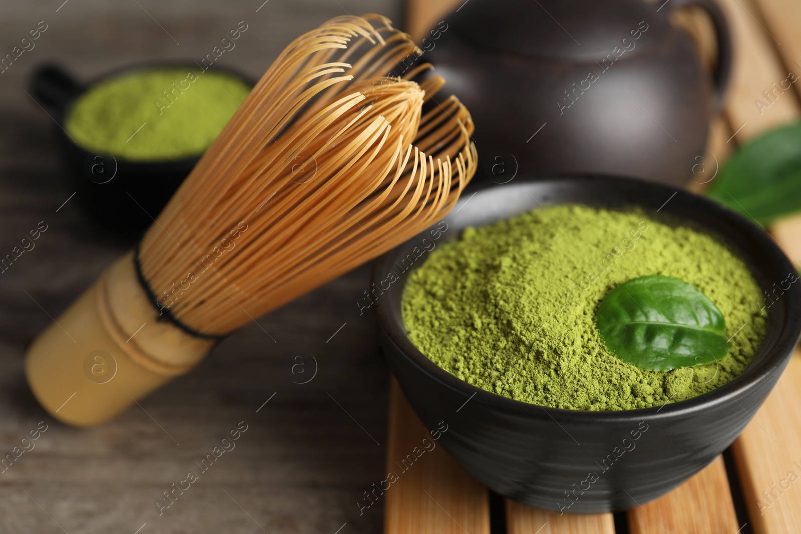 Photo of Green matcha powder and bamboo whisk on wooden table, closeup