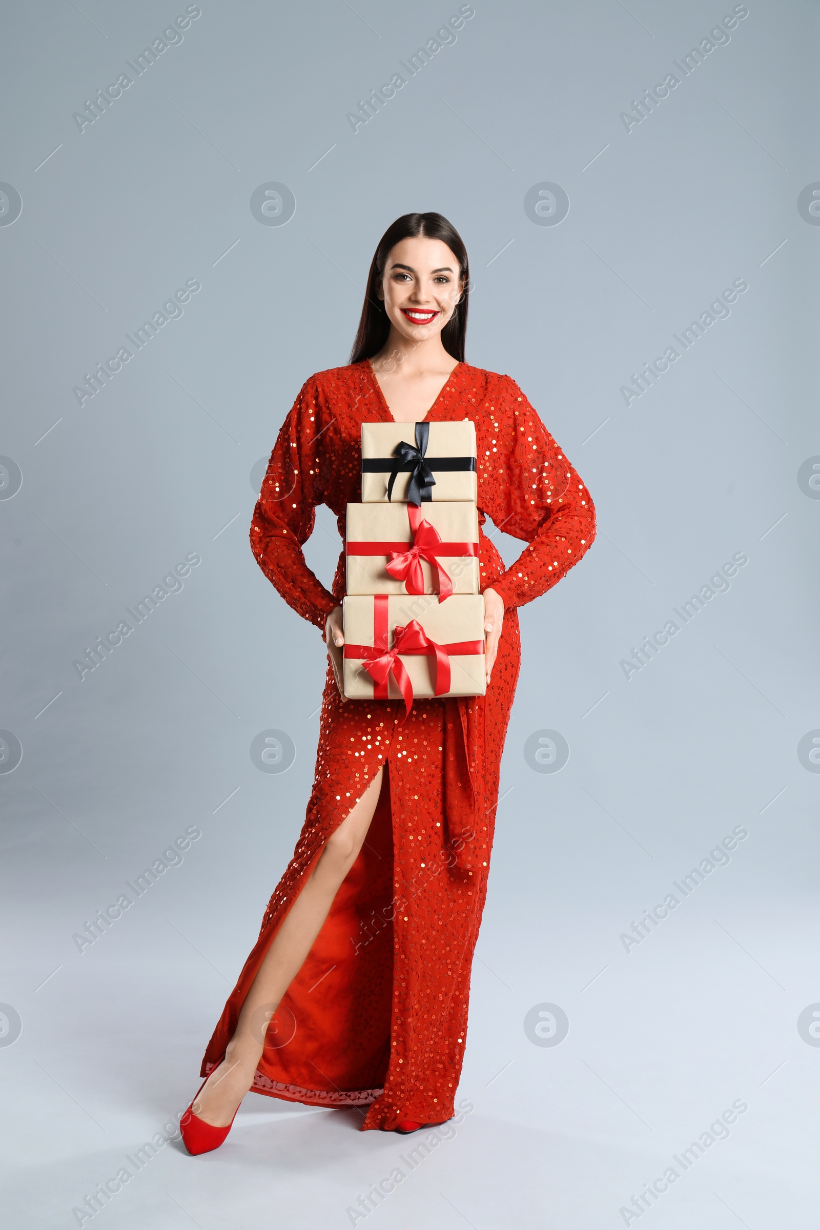 Photo of Woman in red dress holding Christmas gifts on grey background