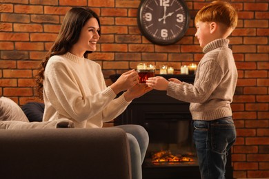 Mother and son with cup of tea near fireplace at home