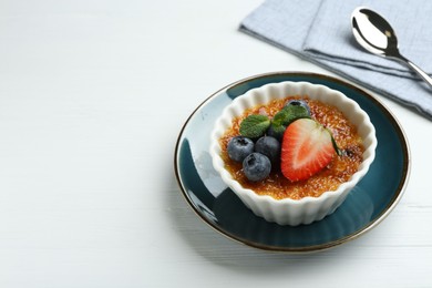 Photo of Delicious creme brulee with berries and mint in bowl on white wooden table, closeup. Space for text