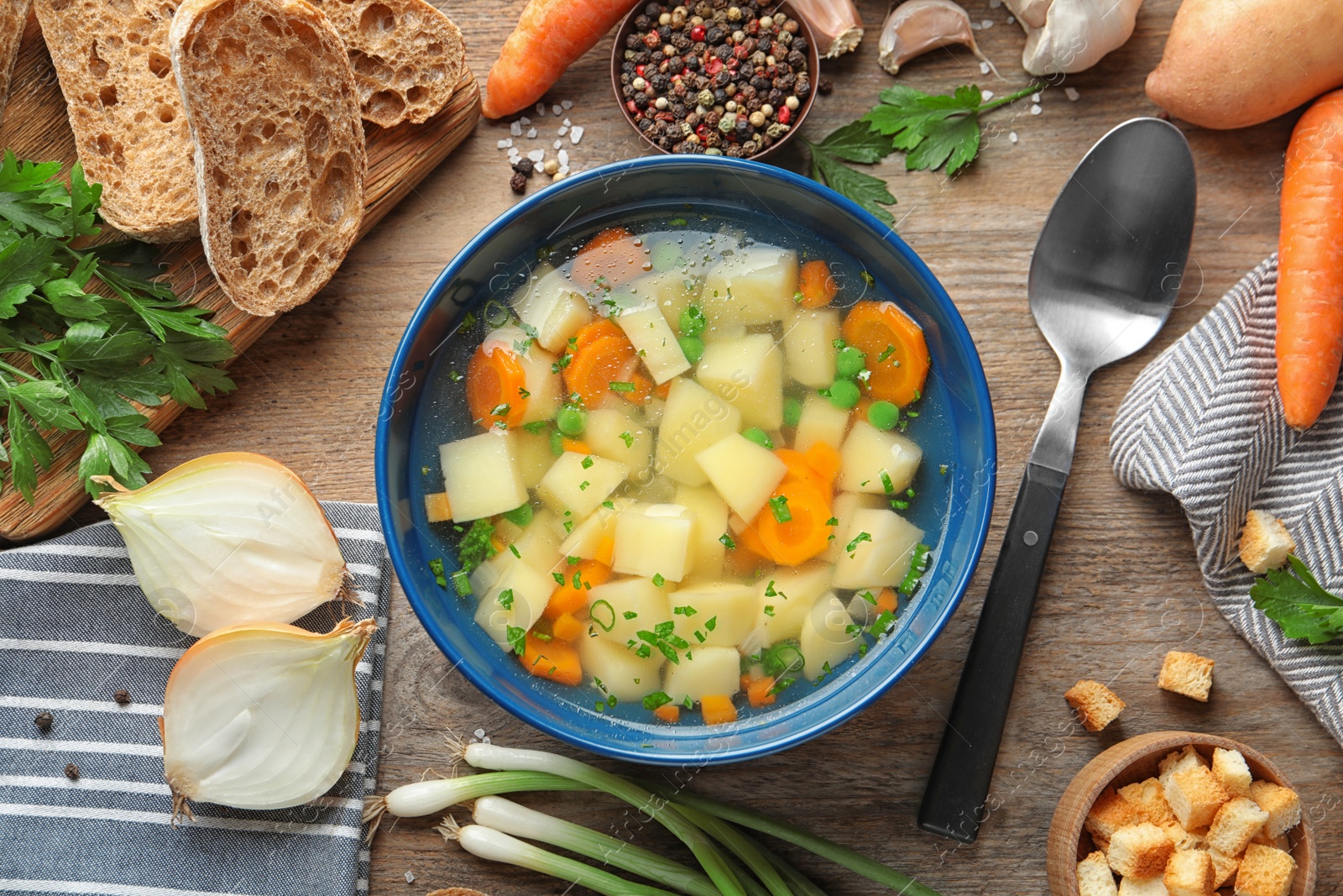 Photo of Bowl of fresh homemade vegetable soup with ingredients on wooden table, flat lay