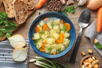 Photo of Bowl of fresh homemade vegetable soup with ingredients on wooden table, flat lay