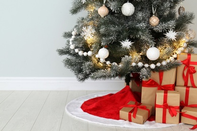 Photo of Decorated Christmas tree with red skirt and gifts indoors