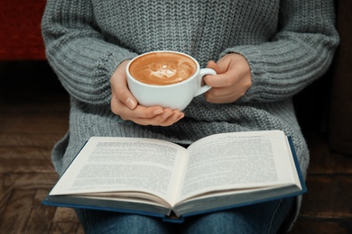 Photo of Woman with cup of coffee reading book at home, closeup