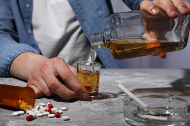 Photo of Alcohol and drug addiction. Man pouring whiskey into glass at grey textured table, closeup