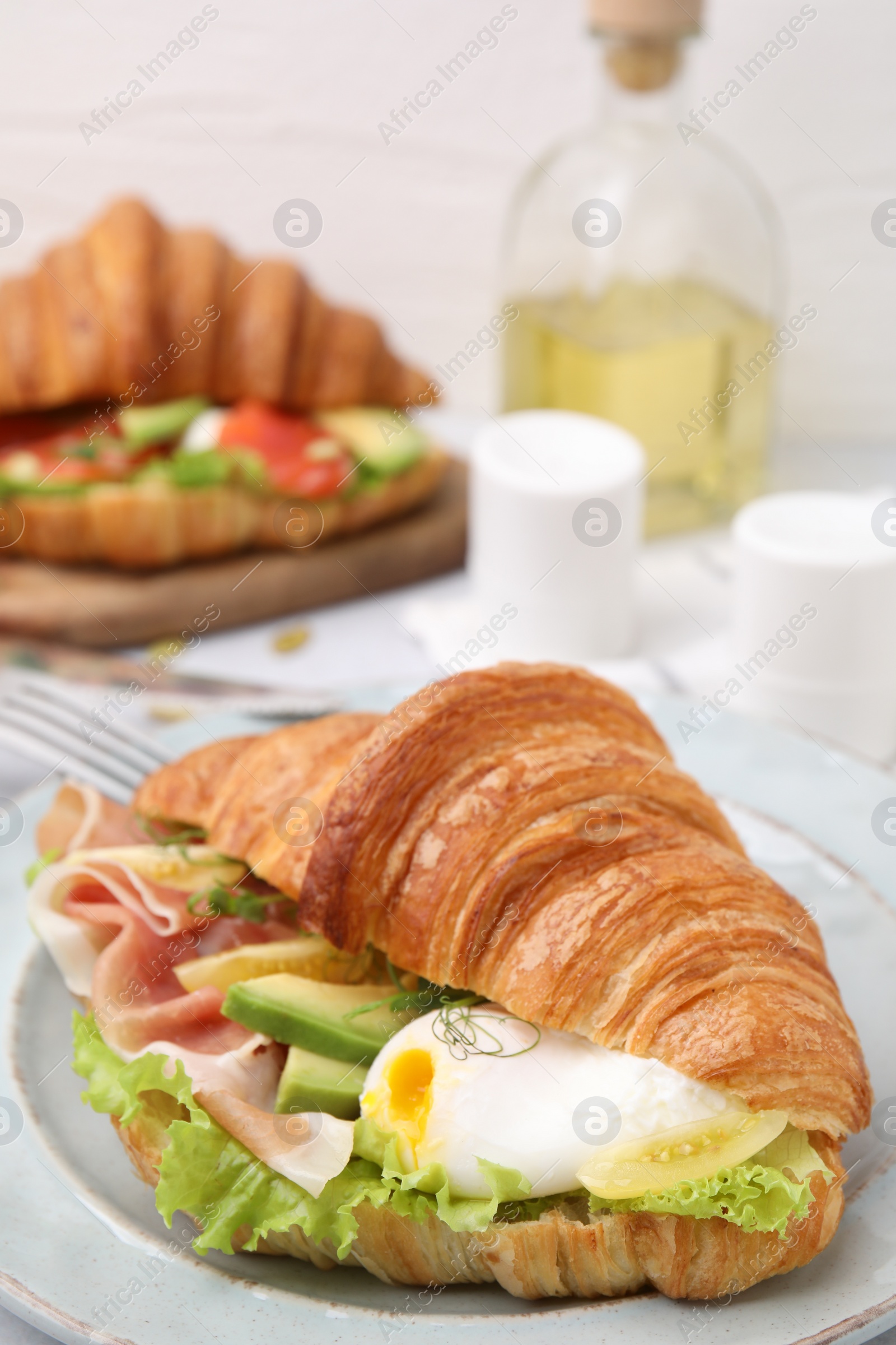 Photo of Delicious croissant with prosciutto, avocado and egg on white table, closeup