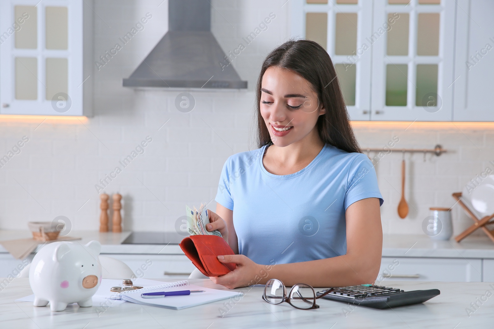 Photo of Young woman counting money at table in kitchen