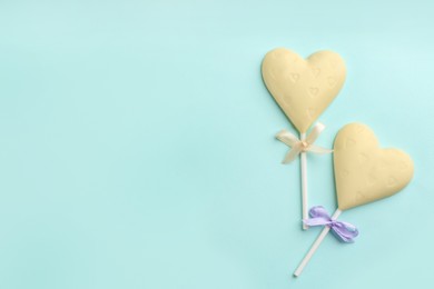 Photo of Chocolate heart shaped lollipops on turquoise background, flat lay. Space for text