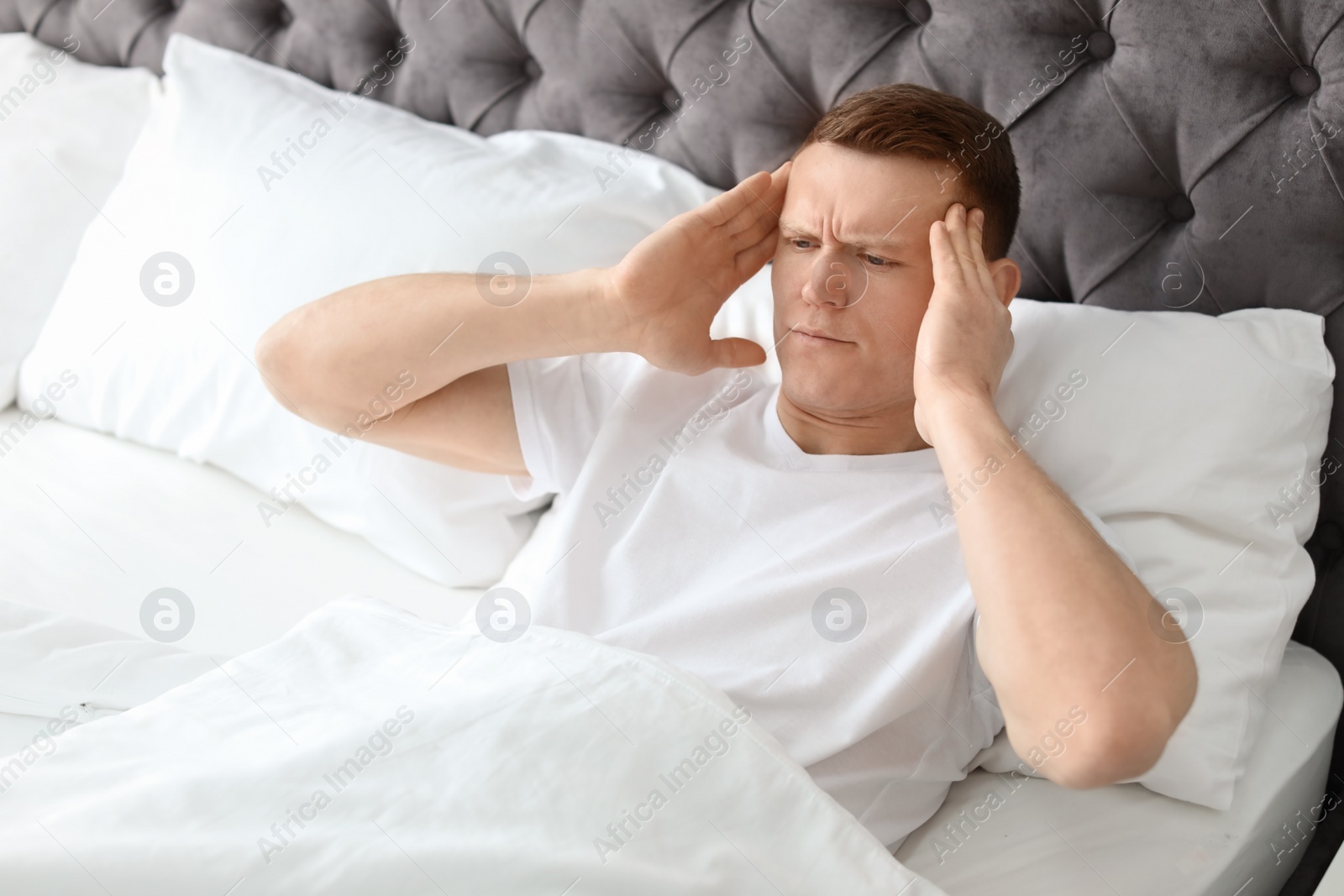 Photo of Young man with headache lying in bed