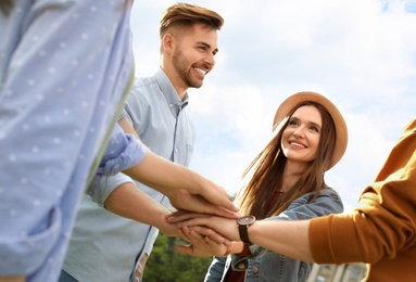 Photo of Happy young people holding hands together outdoors on sunny day, closeup