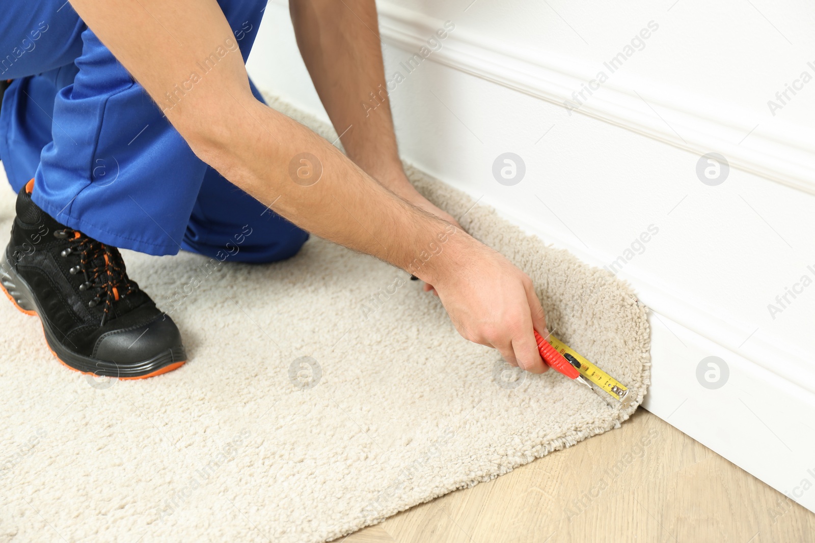 Photo of Worker with cutter knife and measuring tape installing new carpet indoors, closeup