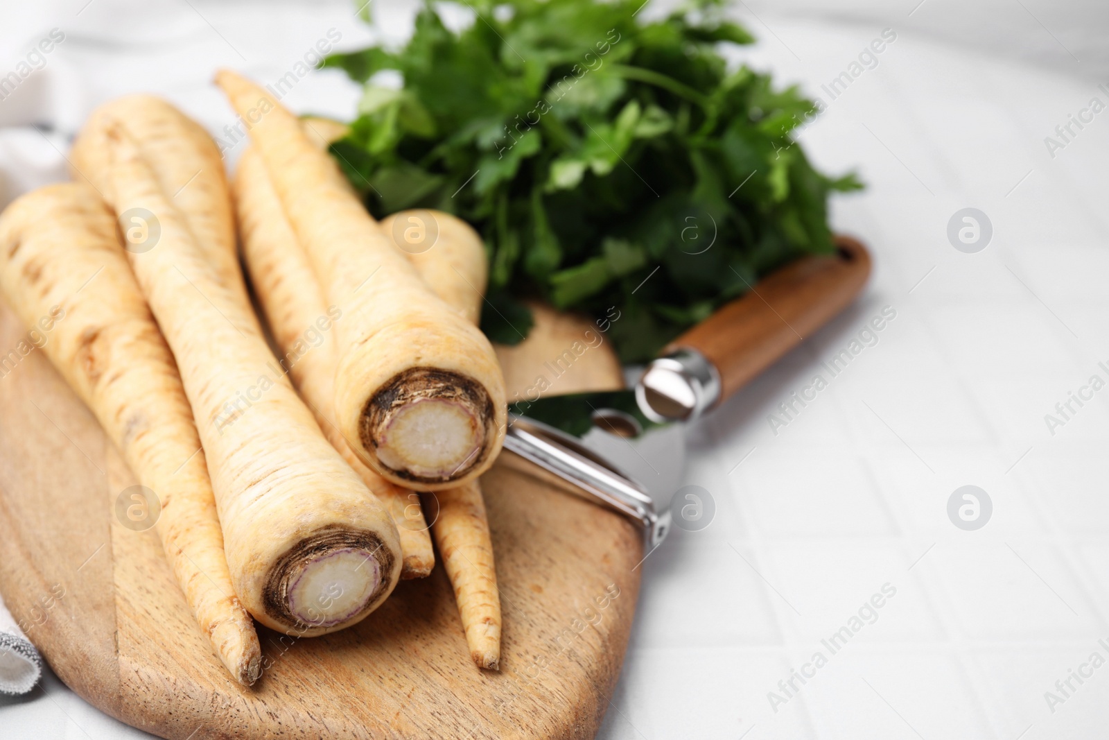 Photo of Whole raw parsley roots and fresh herb on white table, closeup. Space for text