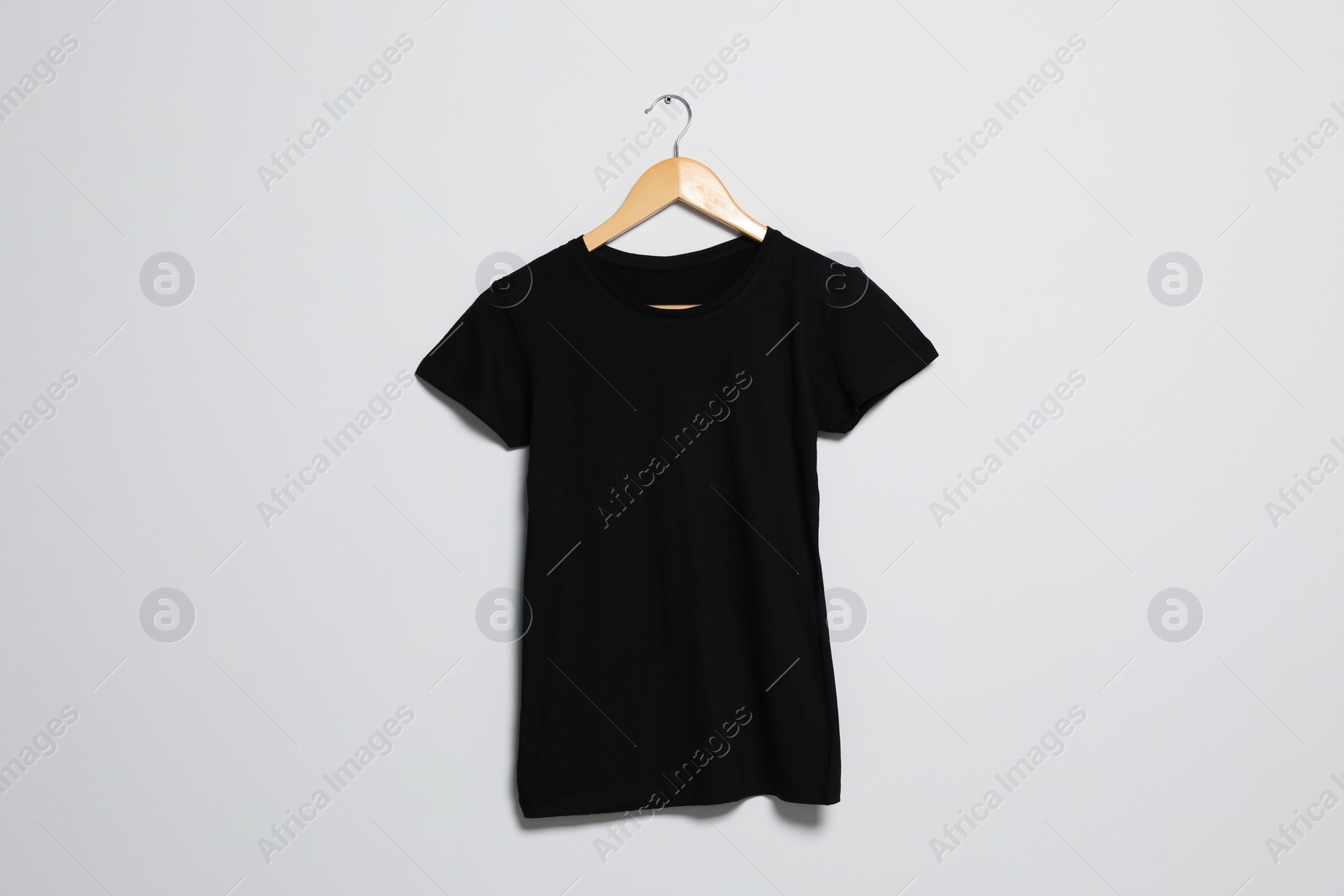 Photo of Hanger with black t-shirt on light wall. Mockup for design