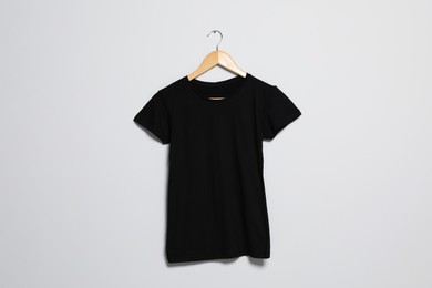 Photo of Hanger with black t-shirt on light wall. Mockup for design