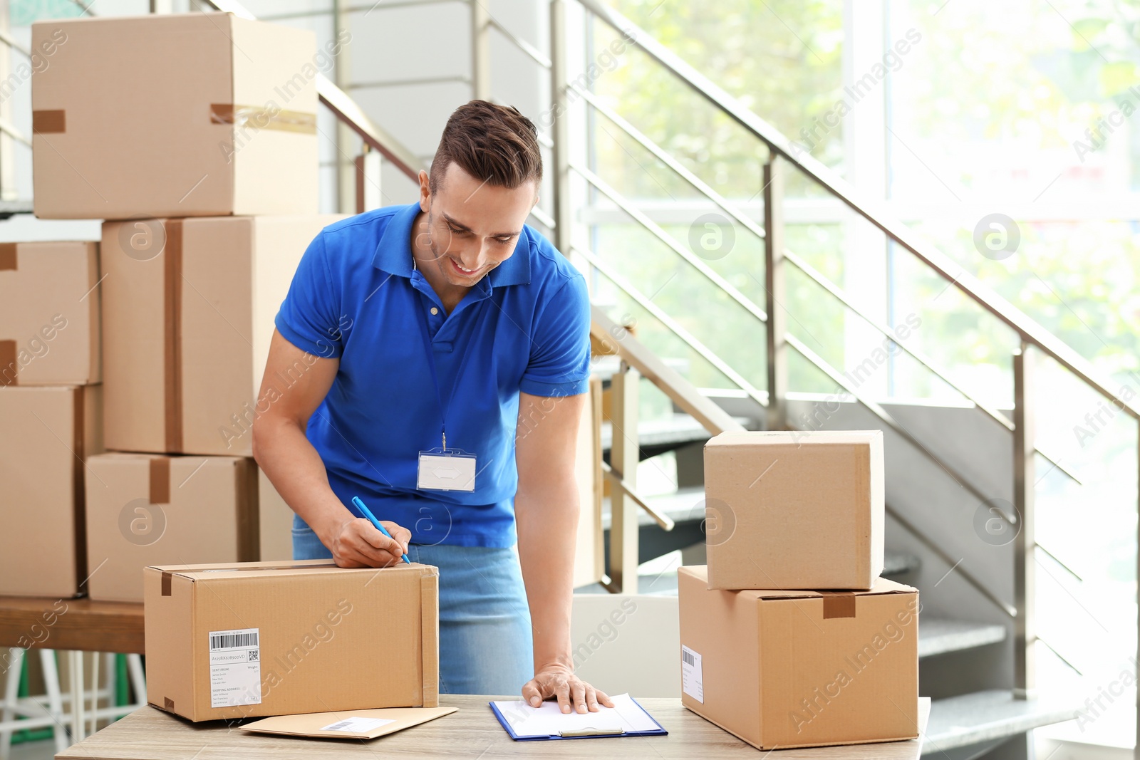 Photo of Young courier making notes on parcels at delivery department