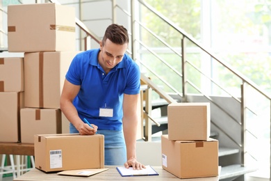 Young courier making notes on parcels at delivery department