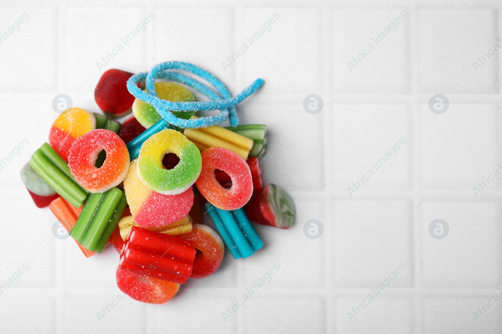 Photo of Pile of tasty colorful jelly candies on white tiled table, flat lay. Space for text