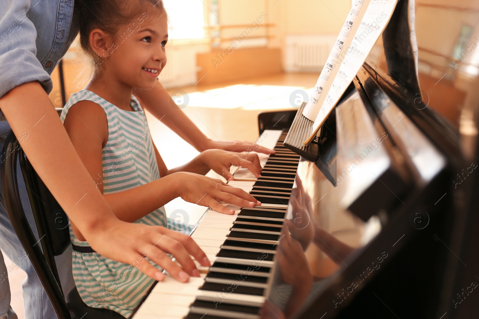 Photo of Young woman teaching little girl to play piano indoors