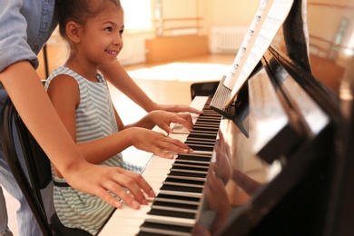 Photo of Young woman teaching little girl to play piano indoors