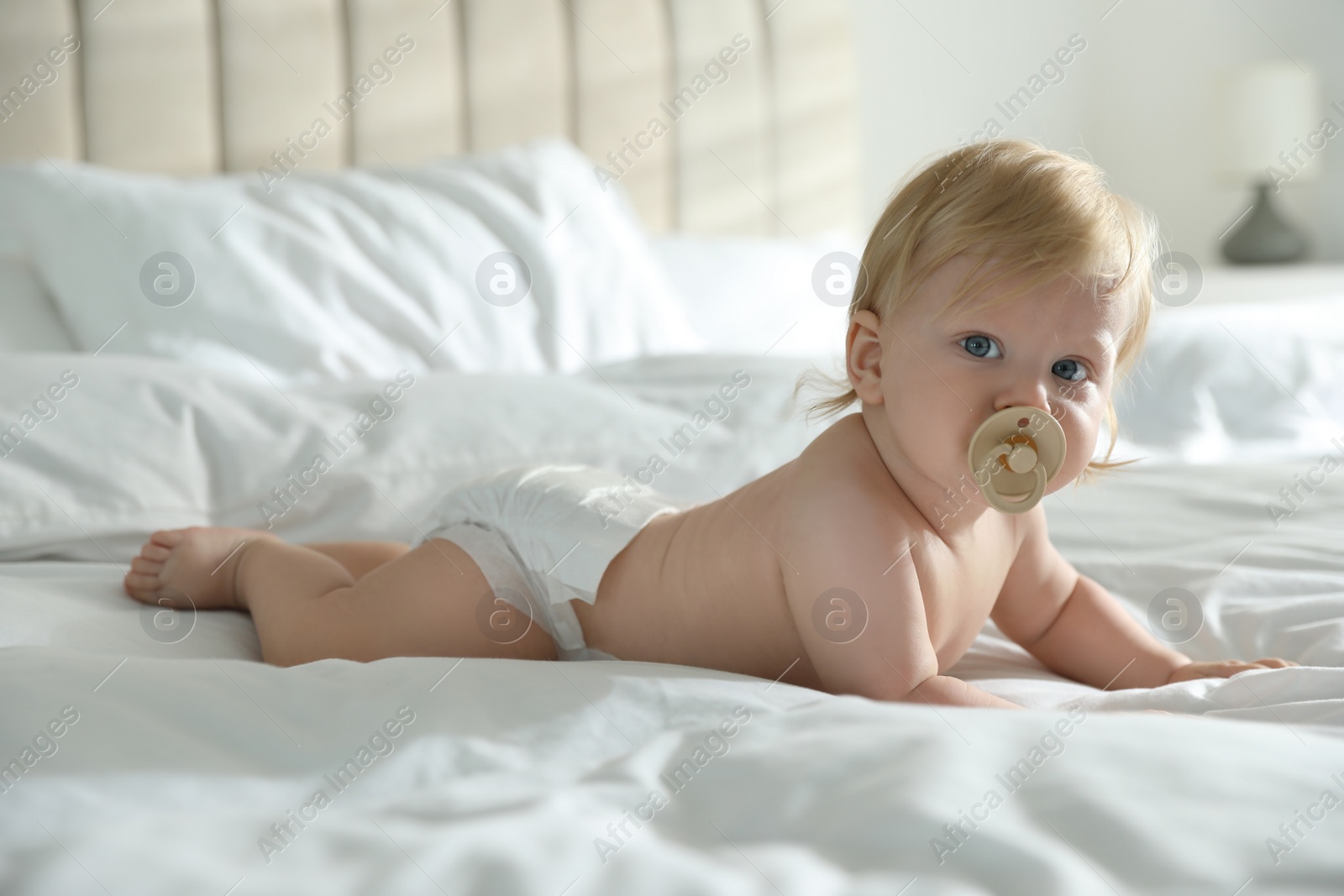 Photo of Cute little baby in diaper with pacifier lying on bed at home