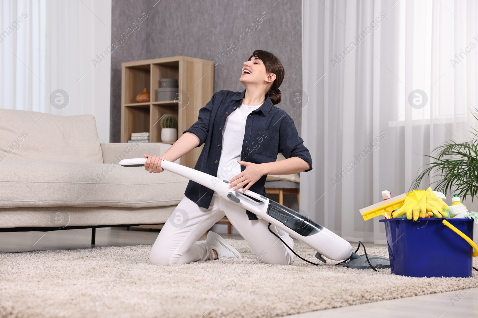 Photo of Happy young housewife having fun while cleaning carpet at home