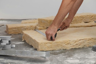 Photo of Worker measuring and cutting insulation material indoors, closeup