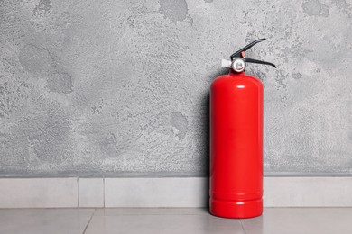 Red fire extinguisher near grey wall, space for text