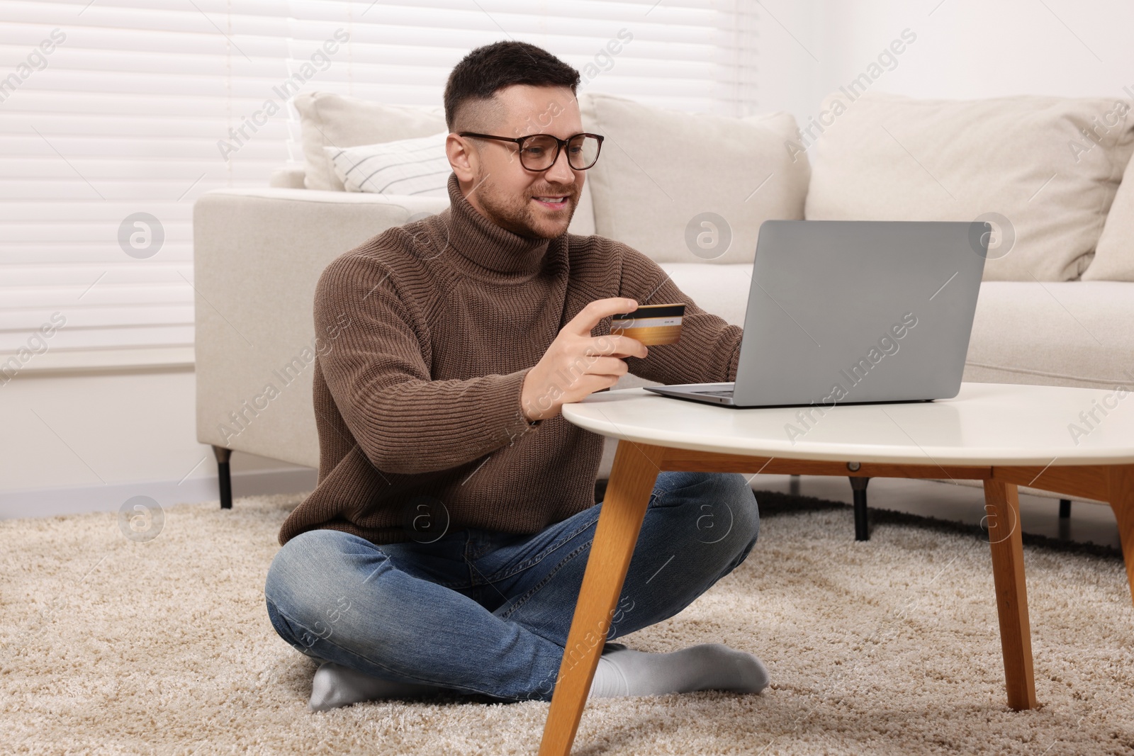 Photo of Handsome man with credit card using laptop for online shopping at home