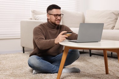 Handsome man with credit card using laptop for online shopping at home