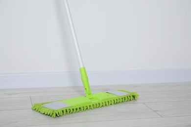 Mop with plastic handle near wall indoors. Space for text