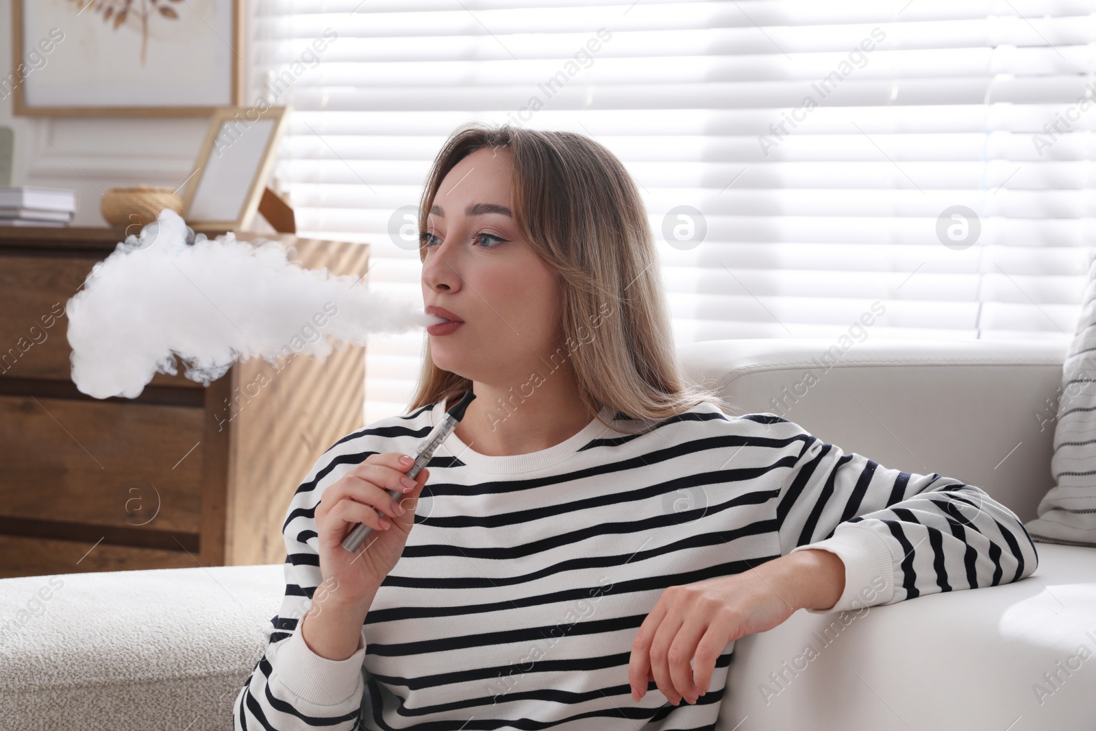 Photo of Beautiful young woman using electronic cigarette at home