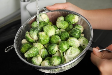 Woman washing Brussels sprouts with running water over sink, closeup