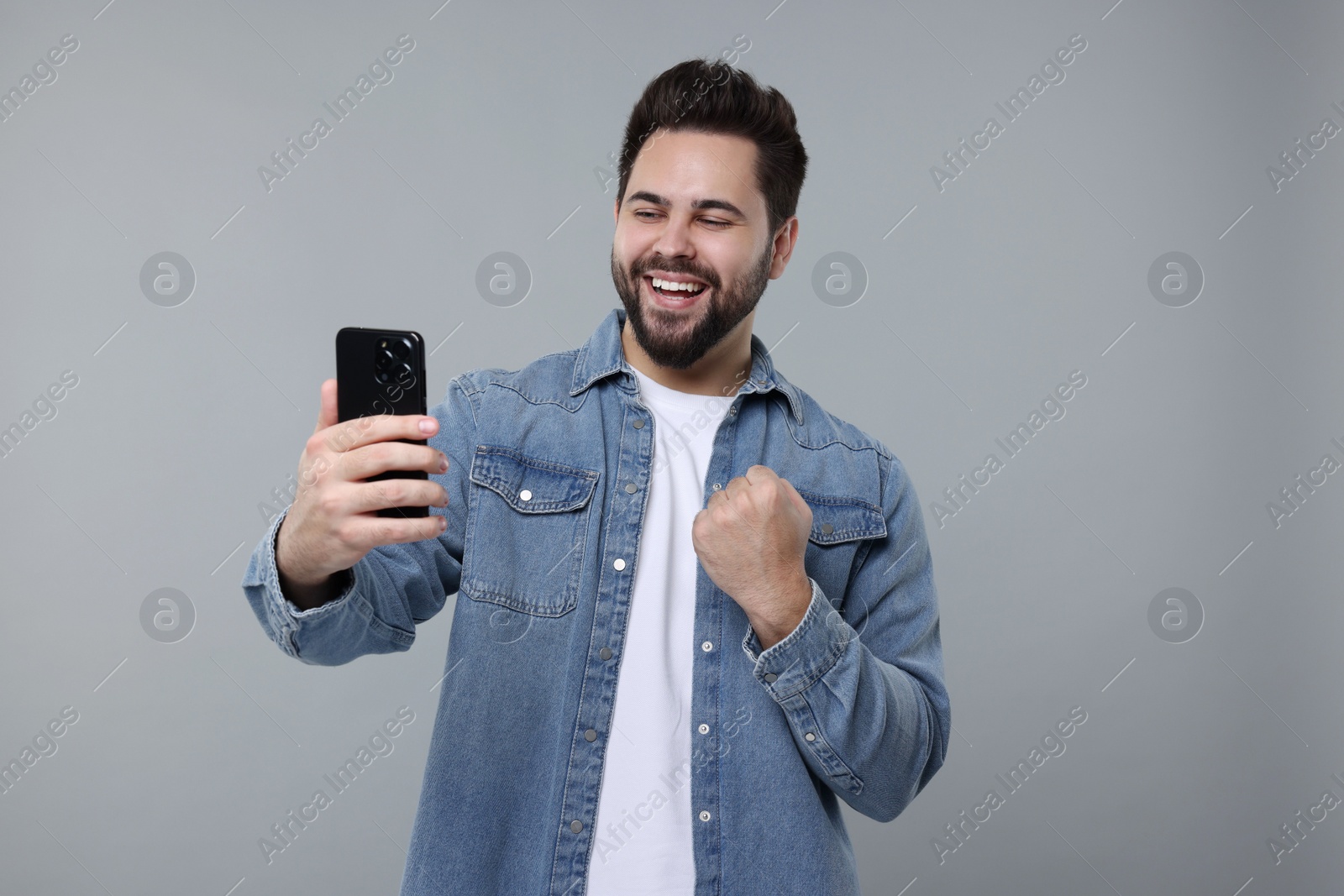 Photo of Happy young man using smartphone on grey background