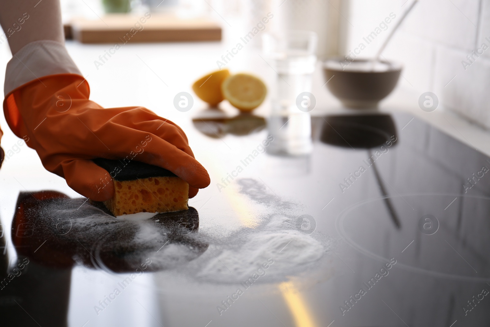 Photo of Woman using baking soda to clean electric cooktop indoors, closeup. Wrong detergent for such surfaces