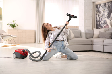 Photo of Young woman having fun while vacuuming at home