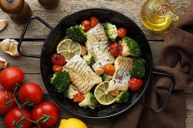 Tasty cod cooked with vegetables in frying pan on wooden table, flat lay