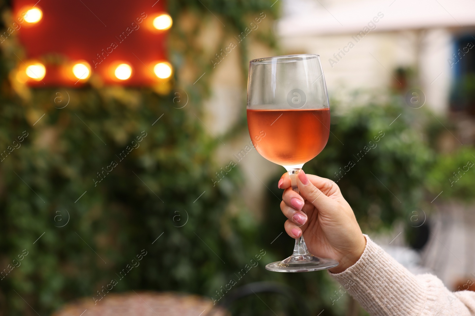 Photo of Woman holding glass of rose wine outdoors, closeup. Space for text