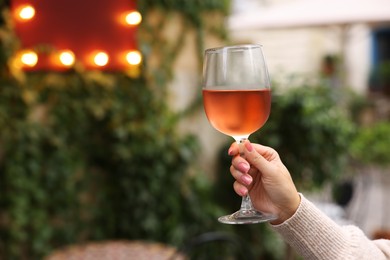 Photo of Woman holding glass of rose wine outdoors, closeup. Space for text