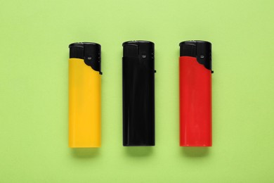 Photo of Stylish small pocket lighters on light green background, flat lay