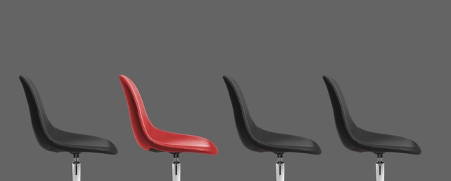 Image of Vacant position. Red office chair among black ones on grey background, banner design