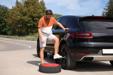Photo of Man changing wheel of car on roadside outdoors