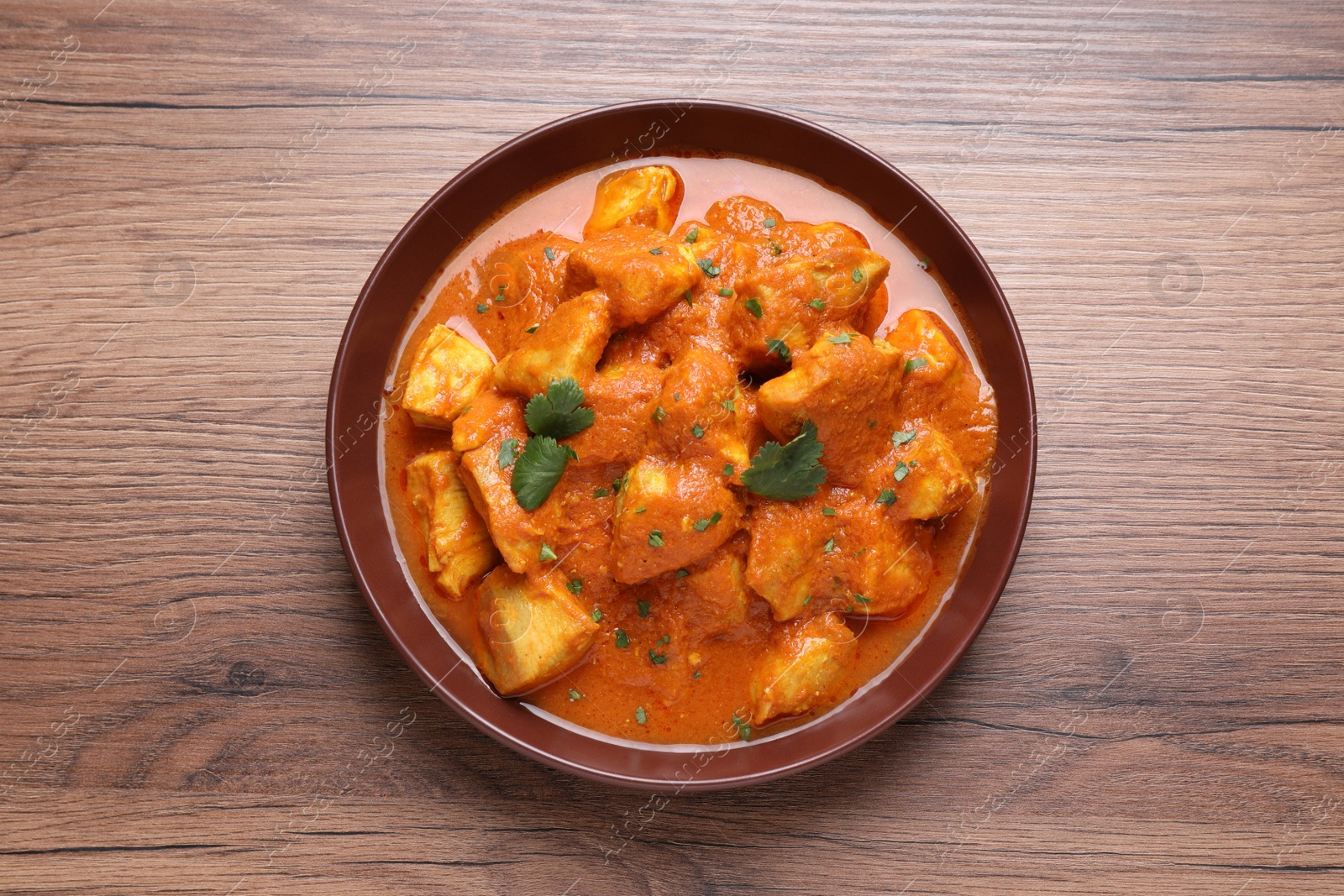 Photo of Bowl of delicious chicken curry on wooden table, top view