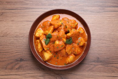 Photo of Bowl of delicious chicken curry on wooden table, top view