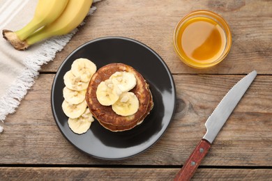 Plate of banana pancakes and honey served on wooden table, flat lay